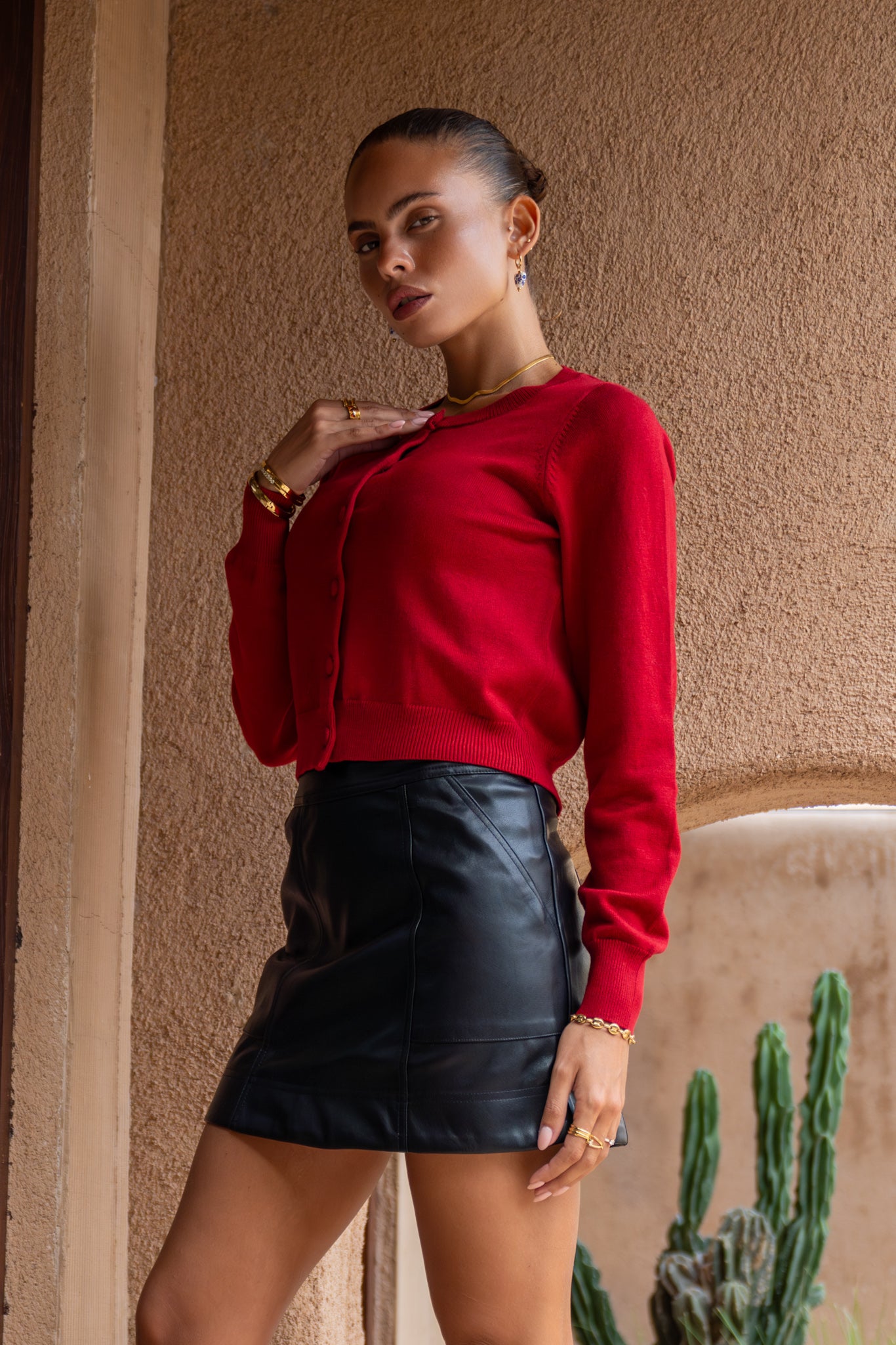 close up side view of woman wearing a red cropped knit cardigan and a black leather mini dress
