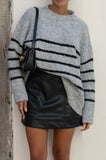 close up of grey black stripe knit sweater, black leather mini dress and black shoulder bag close up of grey black stripe knit sweater, black leather mini dress and black shoulder bag
