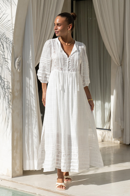 woman wearing a white lace maxi dress in front of curtains