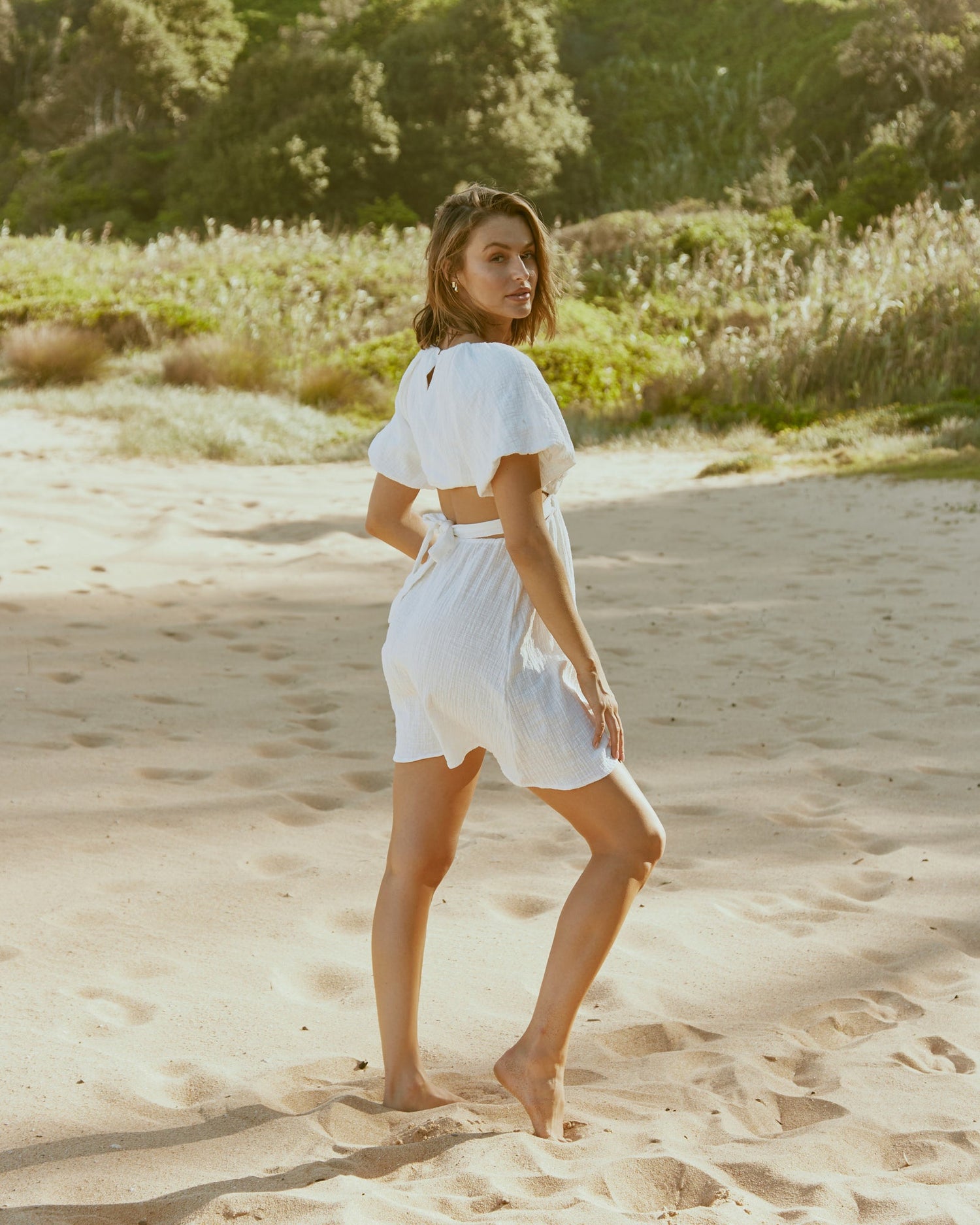 Woman wearing the etta white puffed sleeve mini dress with back cut out at the beach