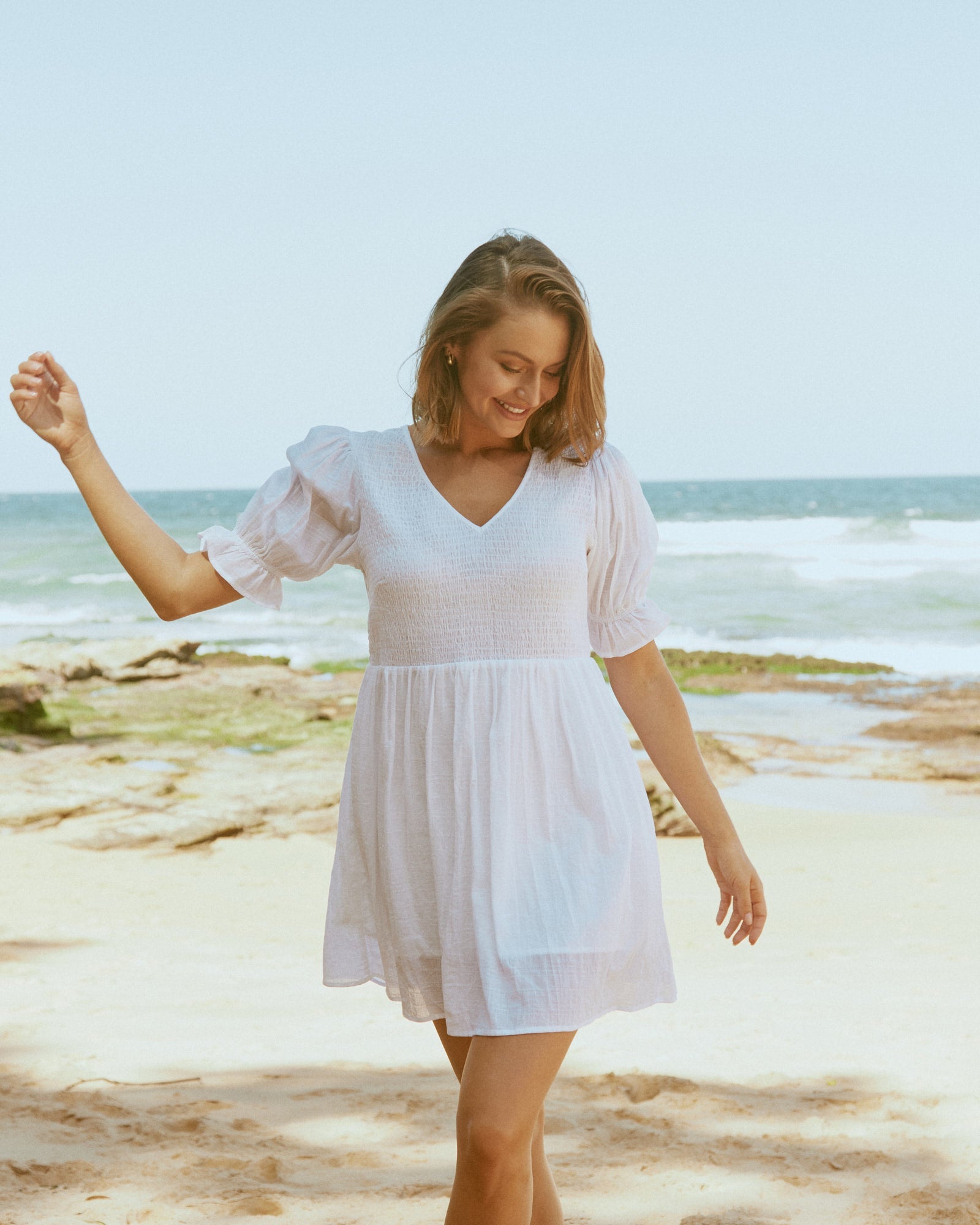 Woman wearing everleigh white puff sleeves mini dress at the beach