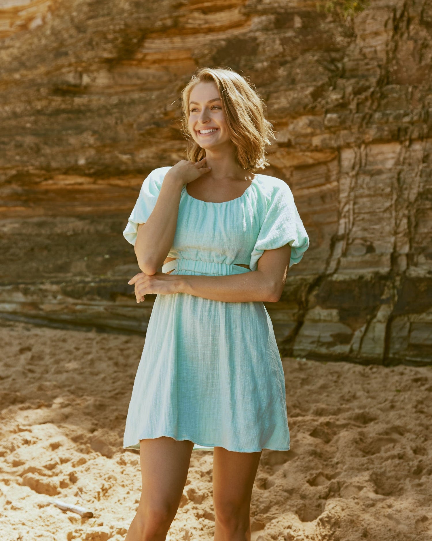 Woman wearing the etta puffed sleeve sage mini dress with back cut out at the beach