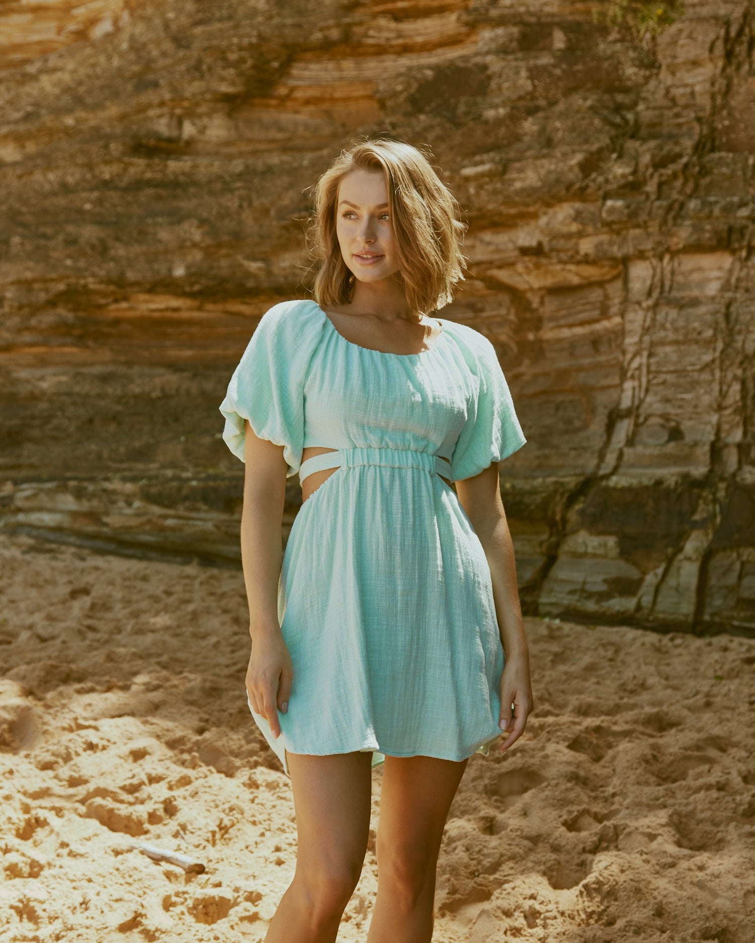Woman wearing the etta puffed sleeve sage mini dress with back cut out at the beach